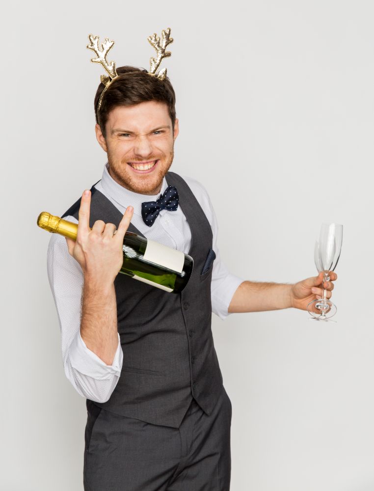 celebration, people and holidays concept - happy man with bottle of champagne and wine glasses at christmas or new year party making rock gesture. man with bottle of champagne at christmas party