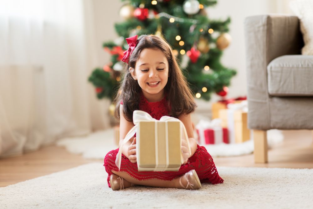 christmas, holidays and childhood concept - happy girl with gift box at home. happy girl with christmas gift at home
