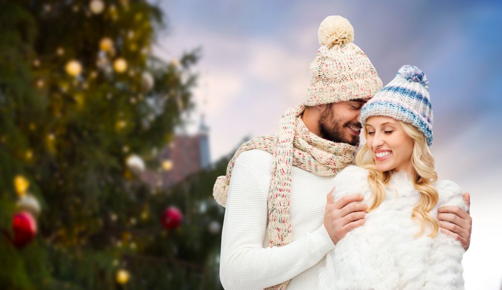 winter and holidays concept - happy couple in hats hugging over christmas tree at tallinn old town hall square background. happy couple hugging over christmas tree