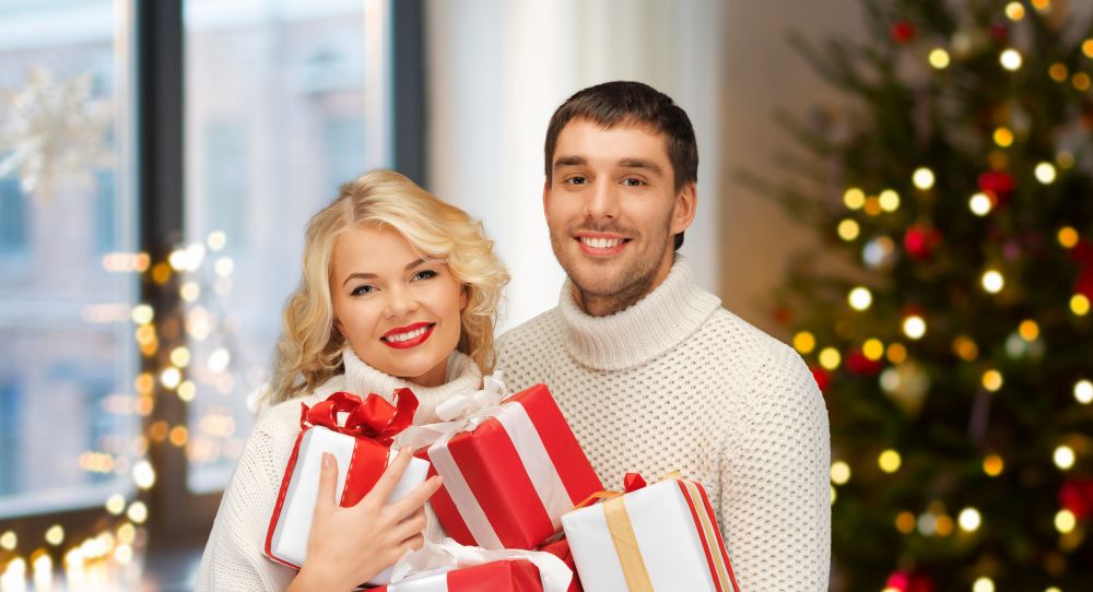 holidays and people concept - happy couple with gifts at home over christmas tree lights background. happy couple with christmas gifts at home