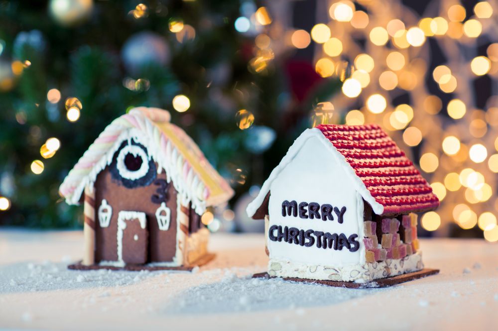 holidays, christmas, baking and sweets concept - close up of beautiful gingerbread houses on white surface with bokeh lights background. close up of christmas gingerbread houses