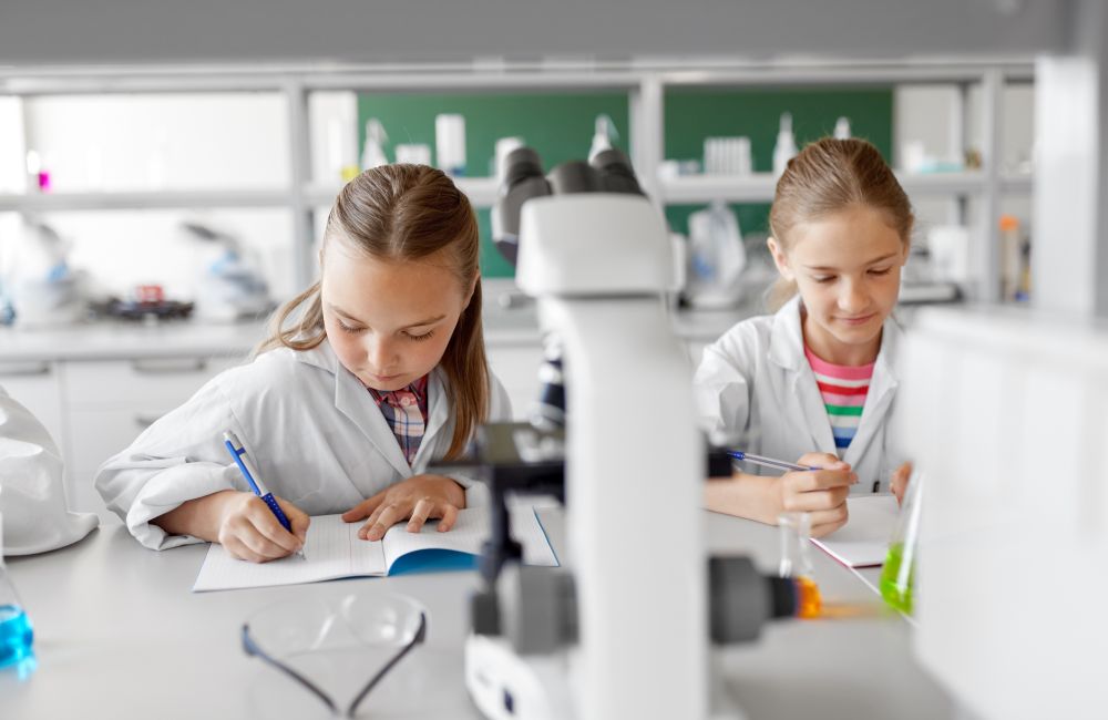 education, science and children concept - kids studying chemistry at school laboratory and writing to workbooks. kids studying chemistry at school laboratory