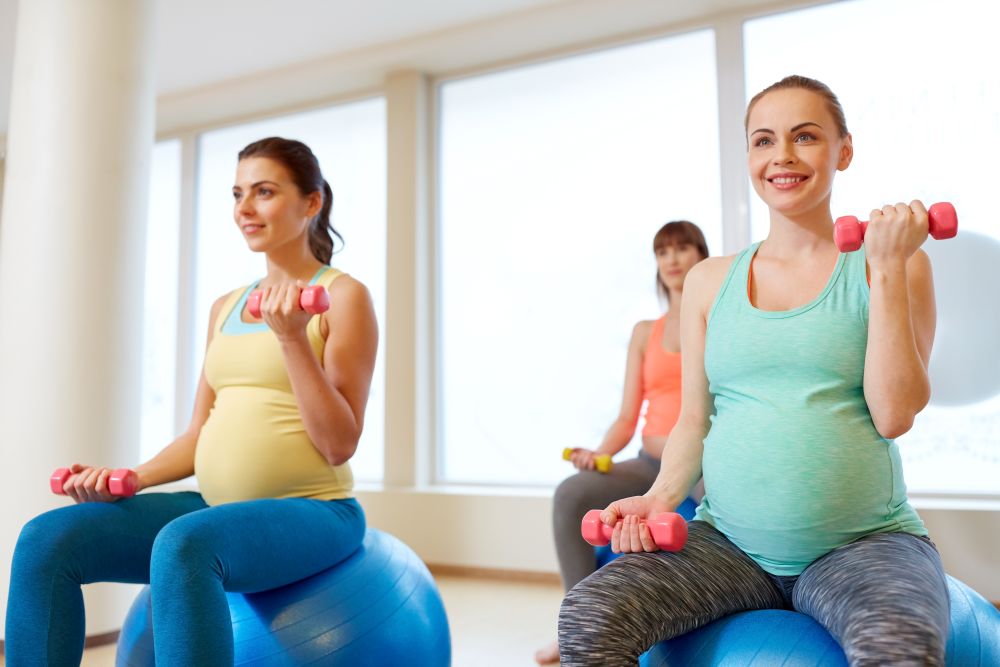 pregnancy, sport, fitness, people and healthy lifestyle concept - group of happy pregnant women with dumbbells on exercise ball in gym. pregnant women training with exercise balls in gym