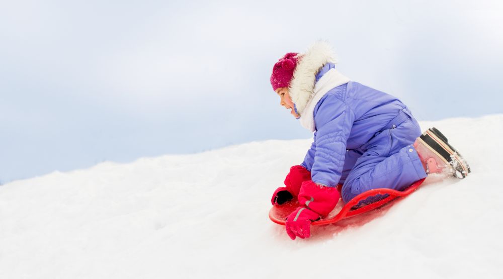 childhood, sledging and season concept - happy little girl sliding down on snow saucer sled outdoors in winter. girl sliding down on snow saucer sled in winter