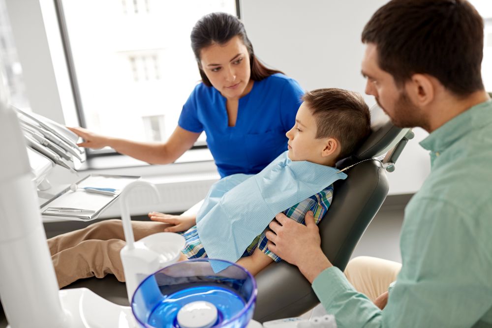 medicine, dentistry and healthcare concept - father and son visiting dentist at dental clinic. female dentist with kid patient at dental clinic