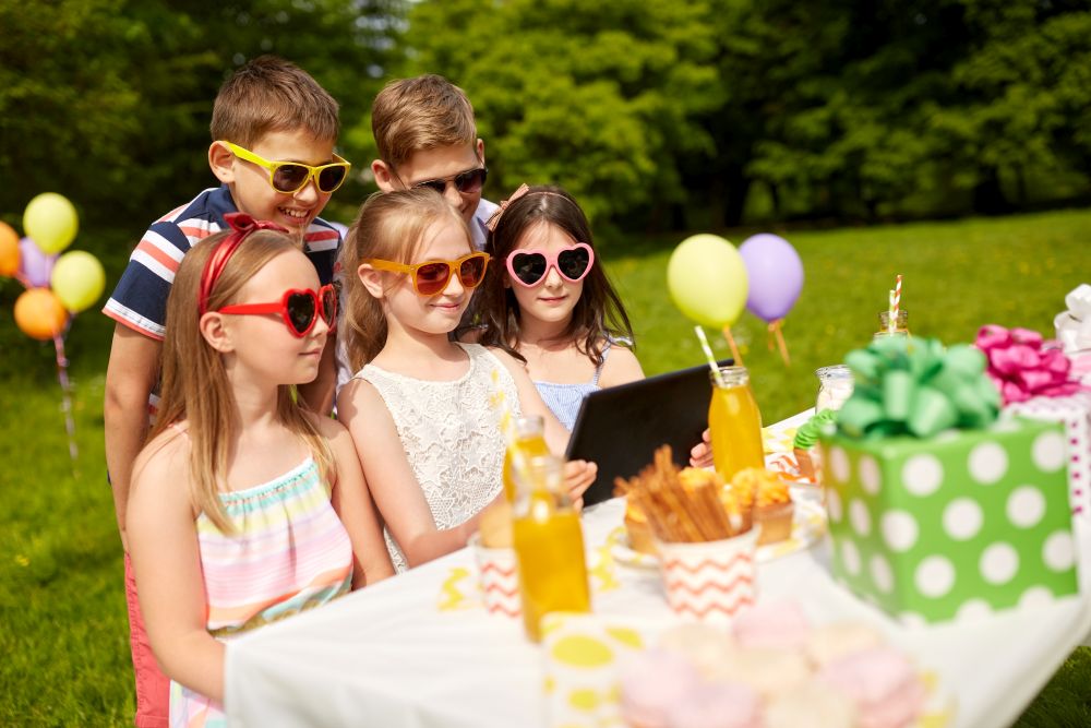 holidays, childhood and technology concept - happy kids in sunglasses with tablet pc on birthday party at summer garden. happy kids with tablet pc on birthday party