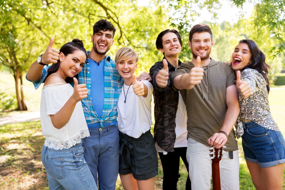 friendship and leisure concept - group of happy friends with guitar showing thumbs up at summer park. friends with guitar showing thumbs up at park