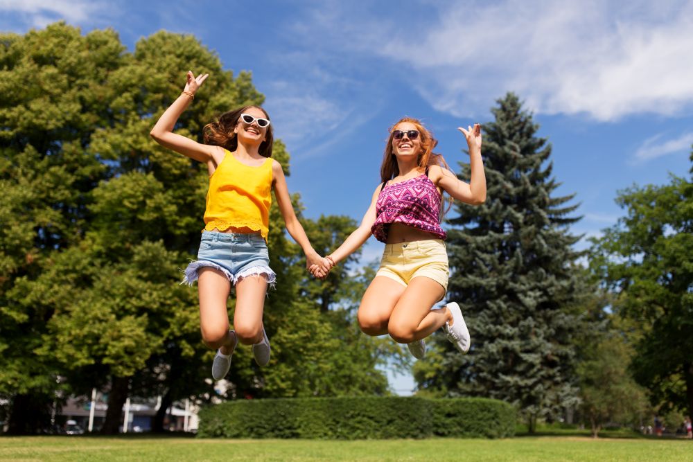 leisure, people and friendship concept - happy teenage girls or friends jumping and having fun at summer park. happy teenage girls jumping at summer park