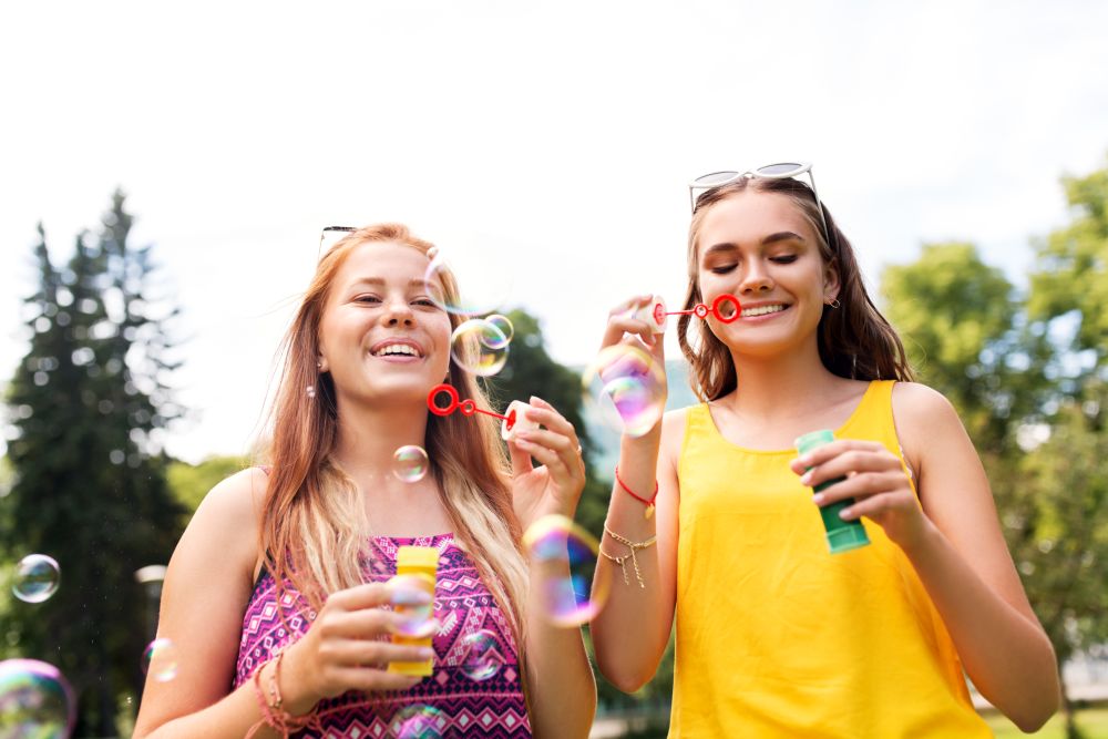 leisure and friendship concept - happy teenage girls or friends blowing bubbles at summer park. teenage girls blowing bubbles at summer park