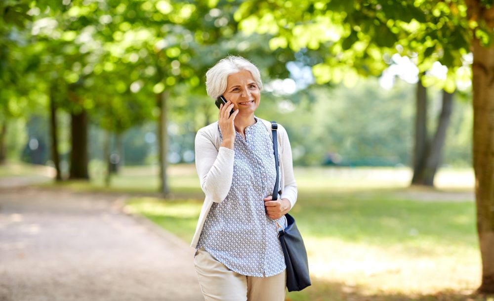 retirement, communication and old people concept - happy senior woman calling on smartphone in summer park. senior woman calling on smartphone in summer park