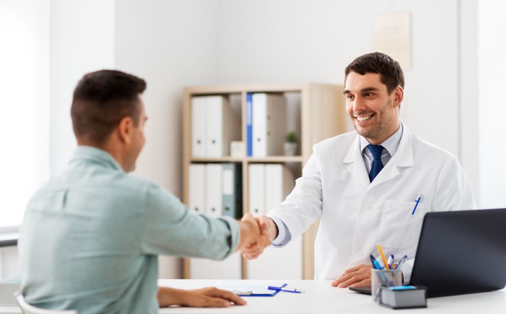 medicine, healthcare and people concept - smiling doctor and male patient shaking hands at hospital. doctor and male patient shaking hands at hospital