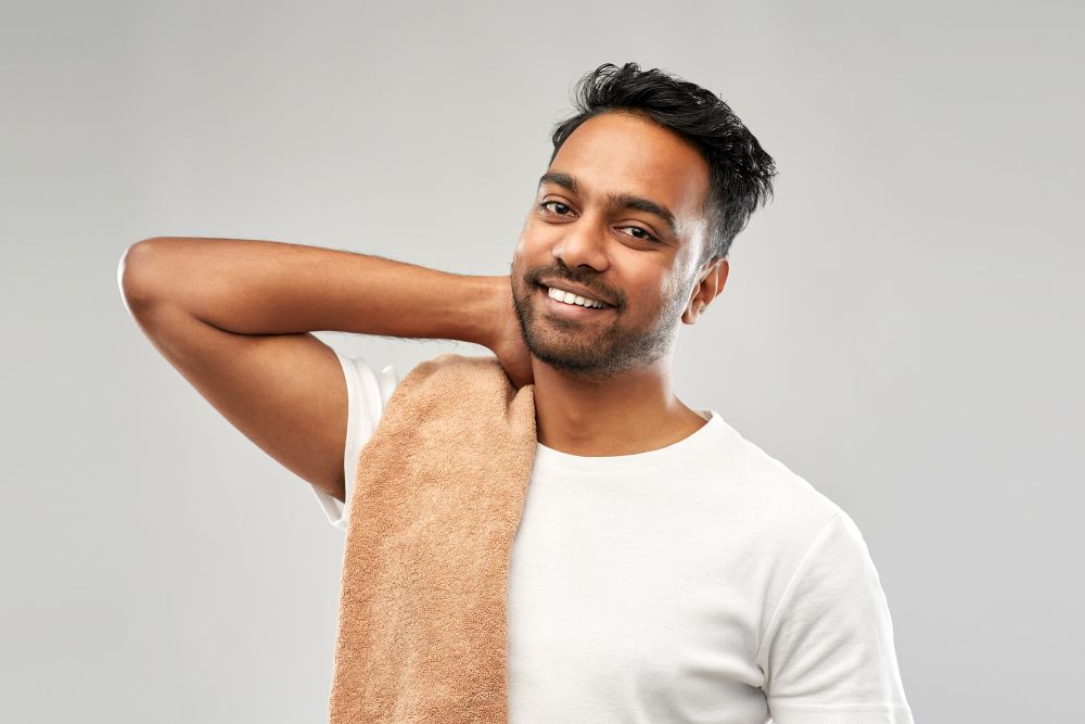 grooming and people concept - smiling indian man with bath towel over grey background. smiling indian man with towel over grey background