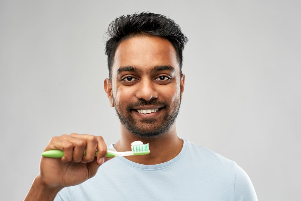 oral care, dental hygiene and people concept - smiling young indian man with toothbrush over grey background. indian man with toothbrush over grey background