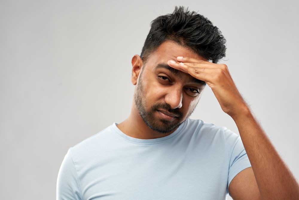 people, health problem and stress concept - unhappy indian man suffering from headache over grey background. unhappy indian man suffering from headache
