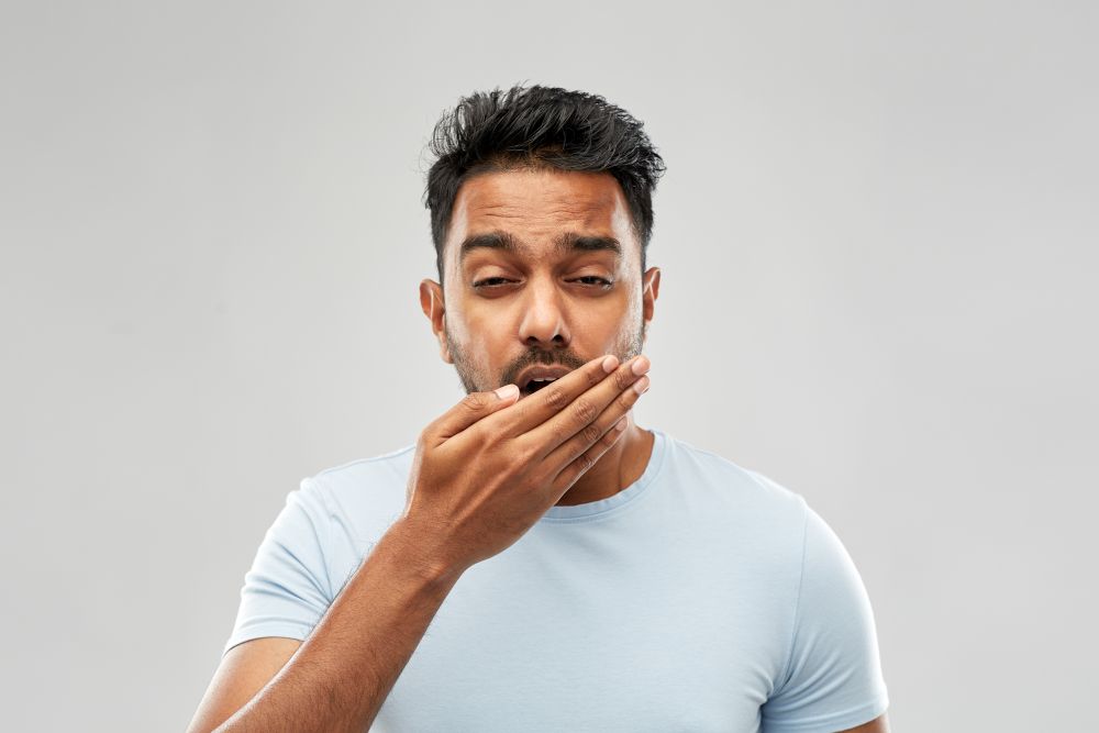 rest, bedtime and people concept - tired indian man yawning over grey background. tired indian man yawning over grey background