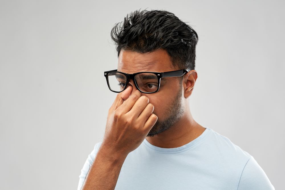 people, vision and overwork concept - tired indian man in glasses rubbing nose bridge over grey background. tired indian man in glasses rubbing nose bridge