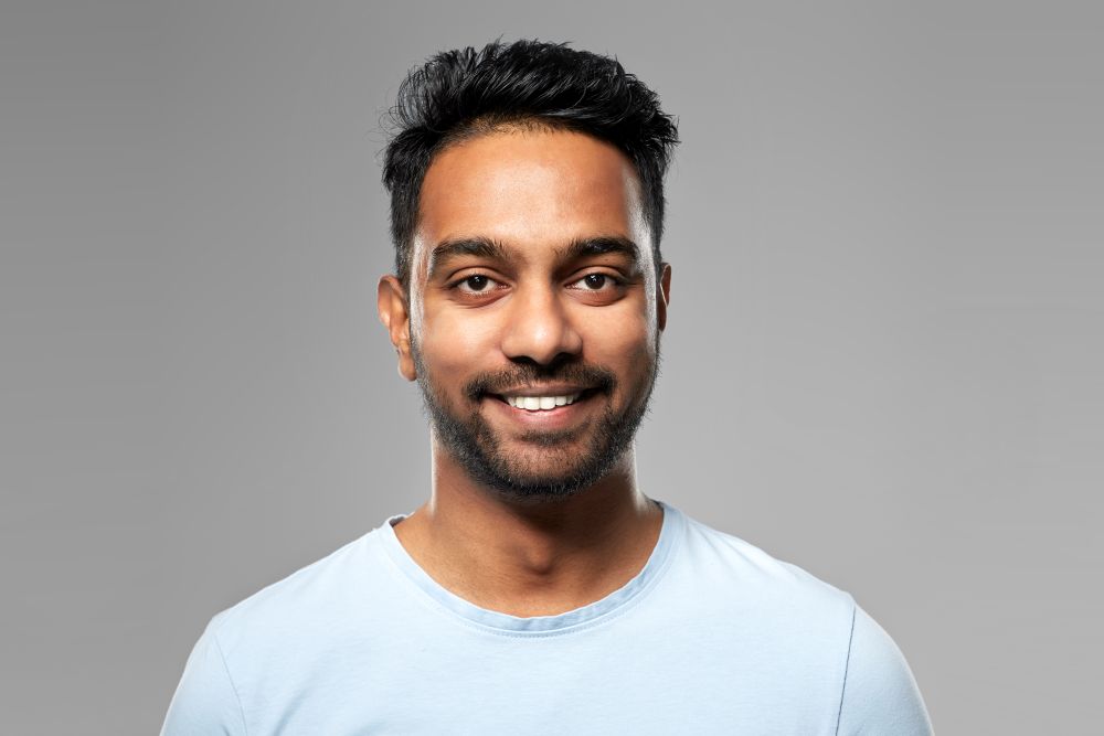 people concept - smiling young indian man over grey background. smiling young indian man over grey background