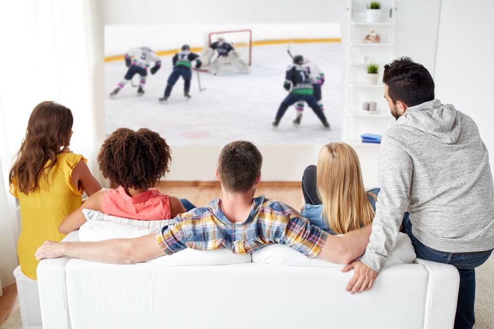 sport, people and entertainment concept - happy friends watching ice hockey game on projector screen at home. friends watching ice hockey on projector screen
