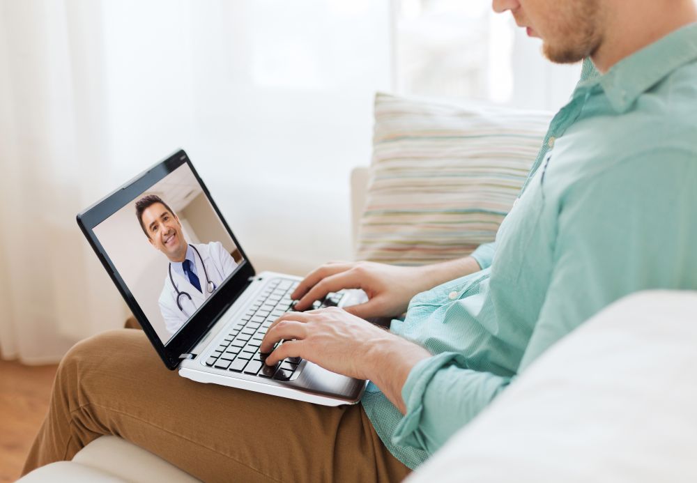 medicine, technology and healthcare concept - close up of man or patient having video call with male doctor on laptop computer at home. patient having video call with doctor on laptop