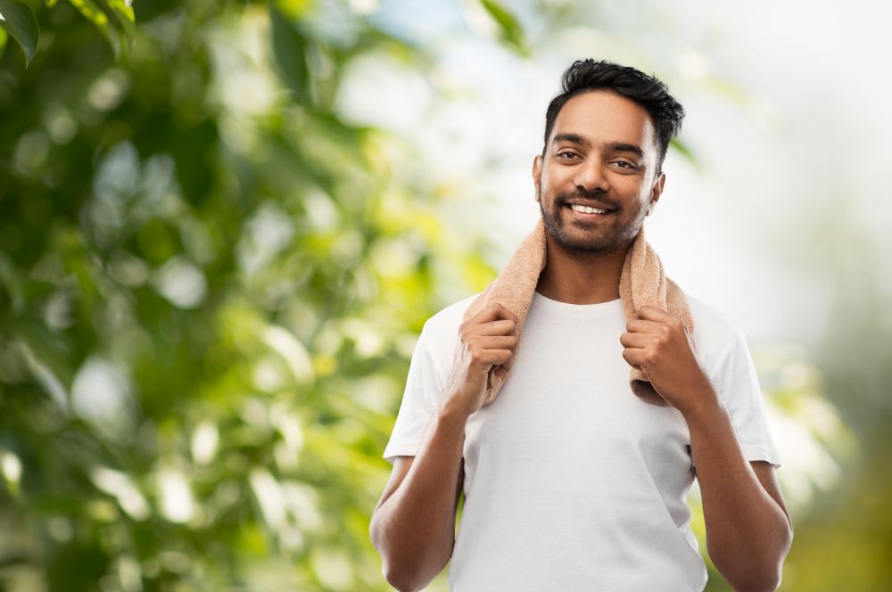 grooming and people concept - smiling indian man with bath towel over green natural background. smiling indian man with towel