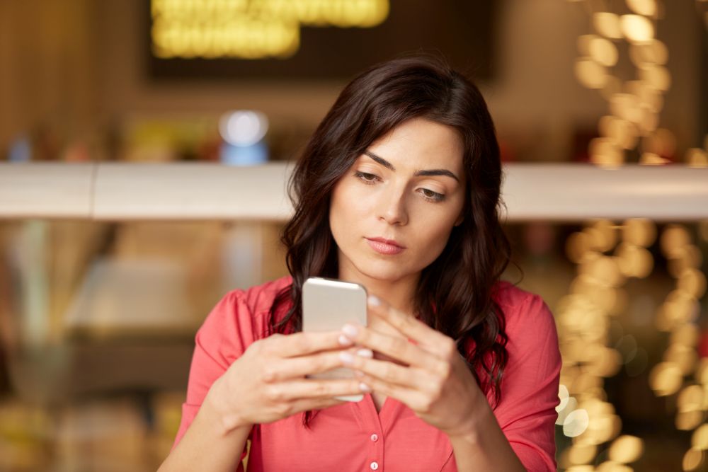 people, technology and leisure concept - woman messaging on smartphone at restaurant. woman with smartphone at restaurant