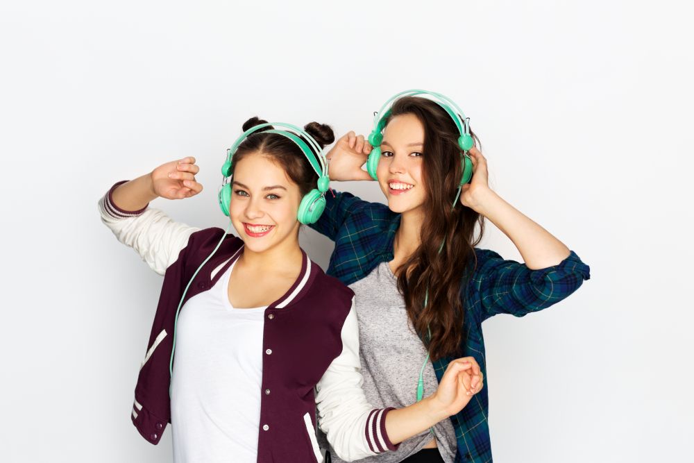 people, leisure and technology concept - smiling teenage girls in earphones listening to music and dancing over white background. teenage girls in earphones listening to music