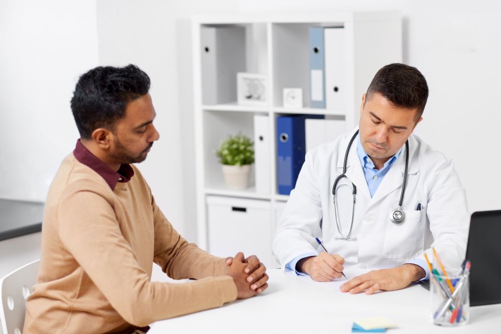medicine, healthcare and people concept - doctor writing prescription for male patient at clinic. doctor and male patient meeting at clinic