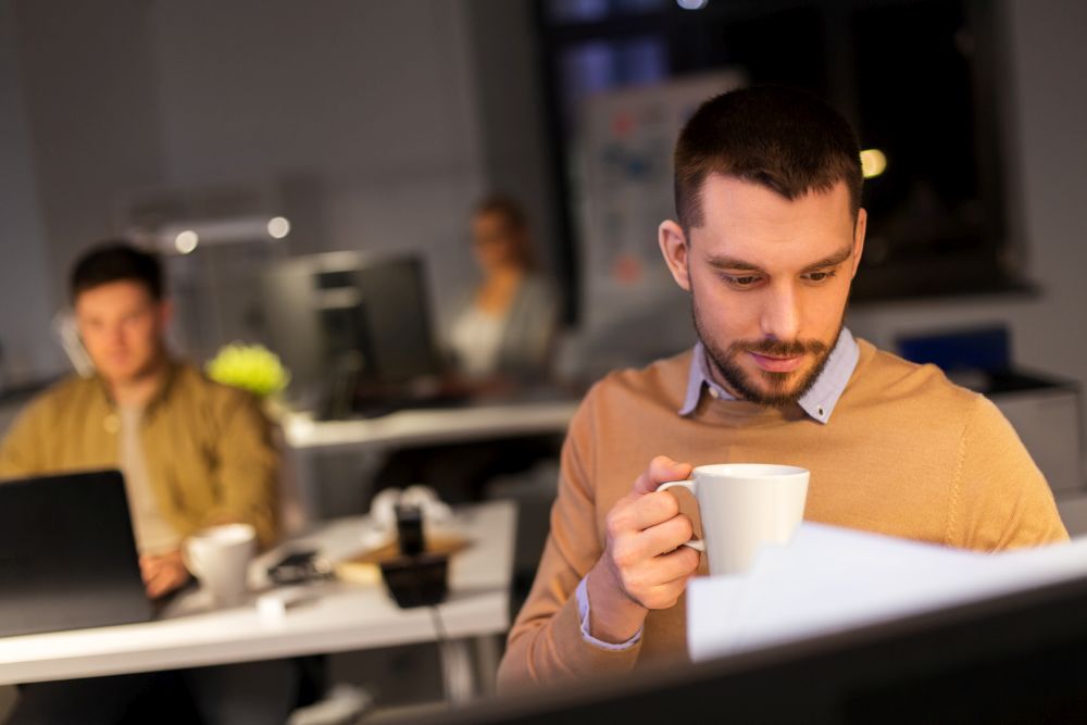 business, overwork and people concept - happy male office worker drinking coffee. happy male office worker drinking coffee