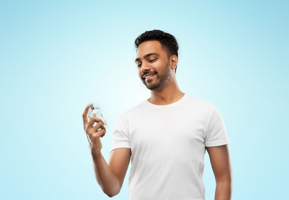 male perfumery, grooming and people concept - happy smiling young indian man with perfume over blue background. happy indian man with perfume over blue background