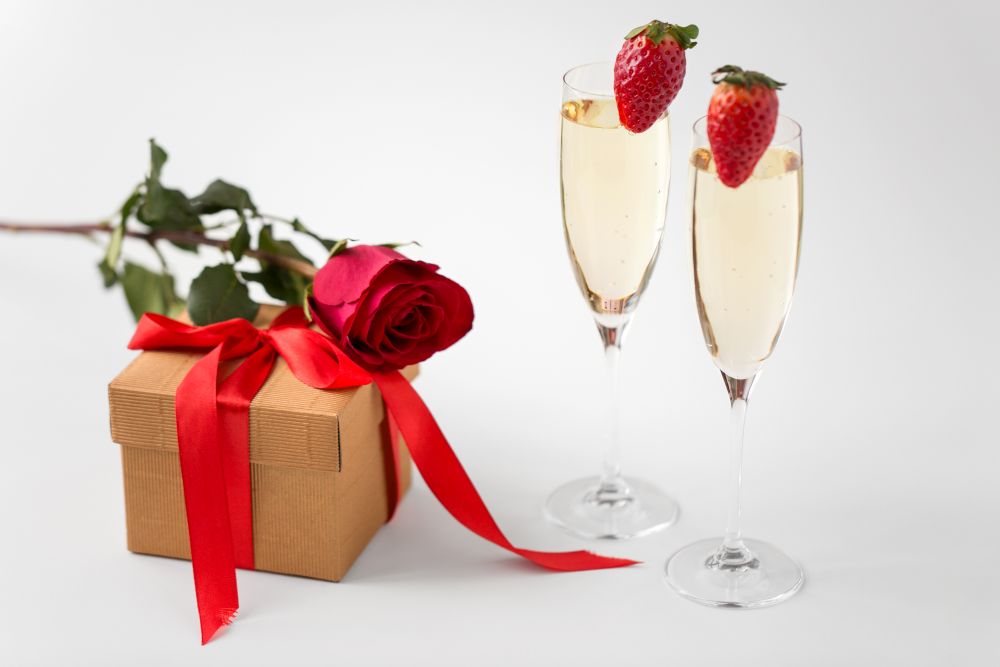 valentines day and holidays concept - two champagne glasses with strawberries and gift box with red rose on white background. two champagne glasses and gift with red rose