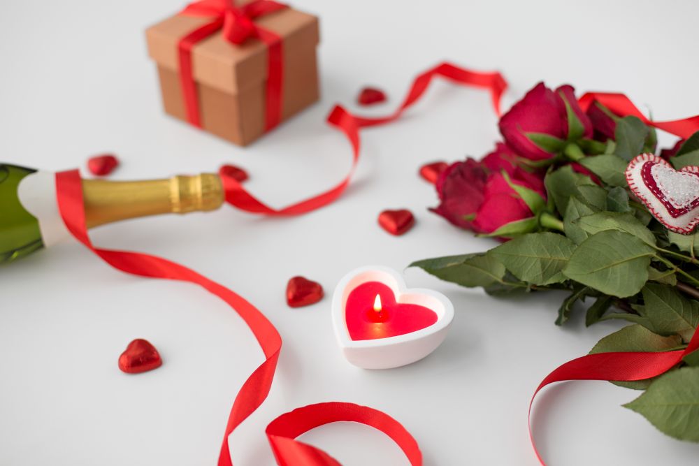 valentines day and holidays concept - close up of champagne, gift, red heart shaped chocolate candies, candle and red roses. close up of champagne, gift, candies and red roses