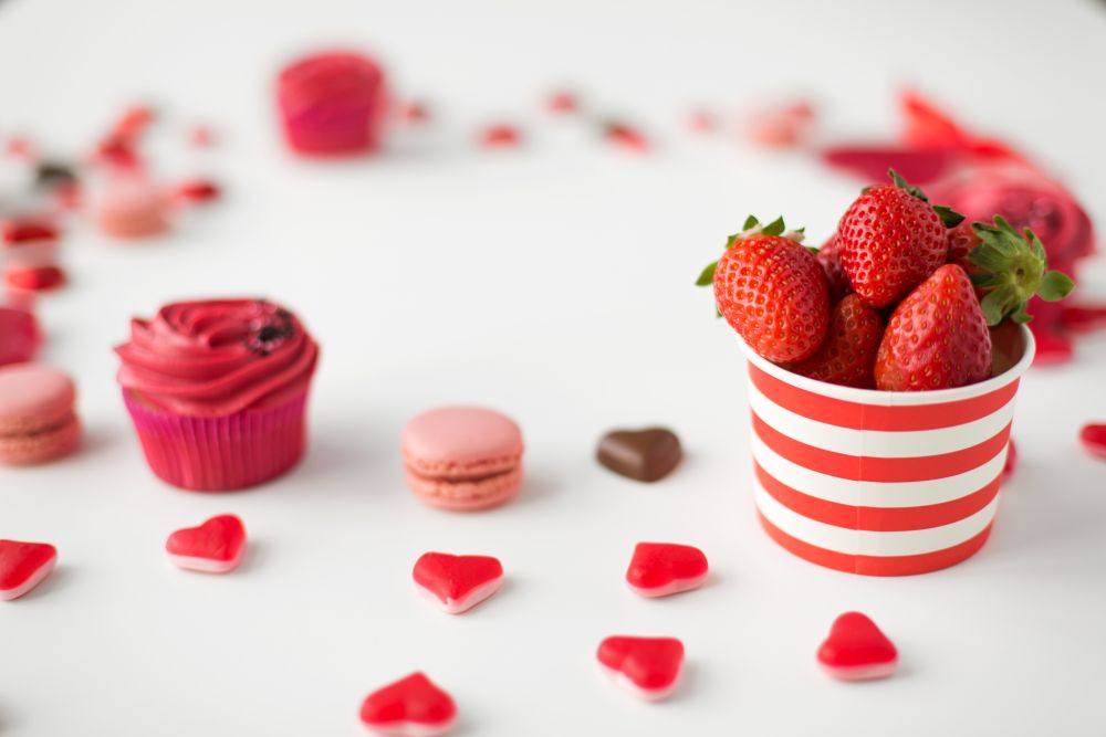 valentines day and sweets concept - close up of strawberries, frosted cupcake, red heart shaped candies and macarons. close up of red treats for valentines day