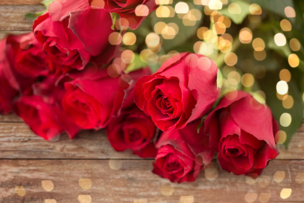 flowers, valentines day and holidays concept - close up of red roses bunch over festive lights. close up of red roses bunch over festive lights