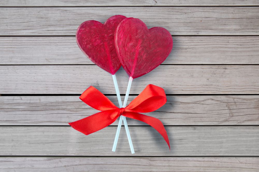 valentines day, sweets and romantic concept - red heart shaped lollipops over grey wooden boards background. red heart shaped lollipops for valentines day