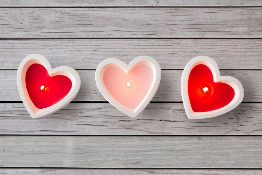 valentines day and decoration concept - heart shaped candles burning over grey wooden boards background. heart shaped candles burning on valentines day