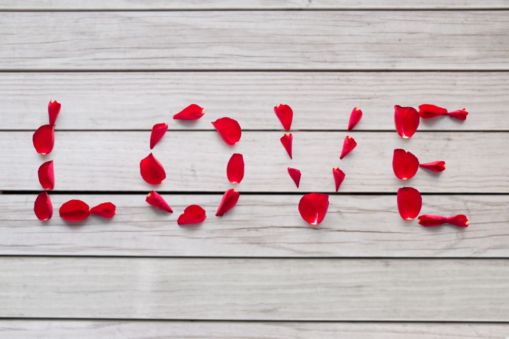 valentines day and romantic concept - word love made of red rose petals over grey wooden boards background. word love made of red rose petals