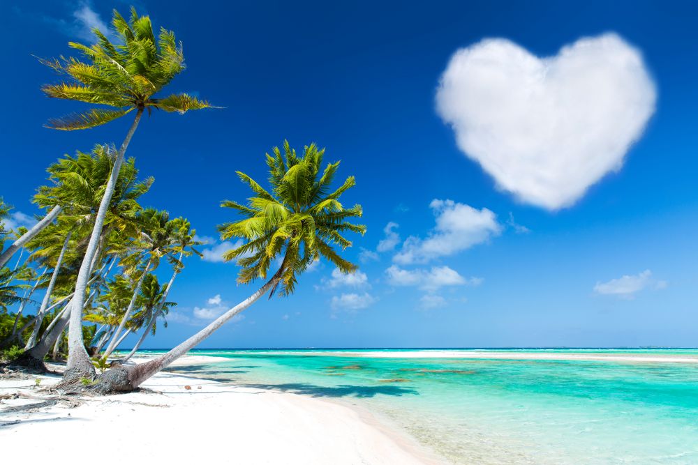 romantic getaway concept - tropical beach with palm trees and heart shaped cloud in french polynesia. romantic beach with palms and heart shaped cloud