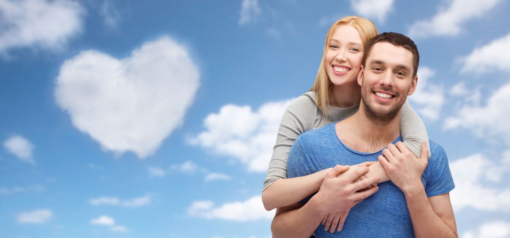 love, valentines day and people concept - smiling couple hugging over blue sky and heart shaped cloud background. couple hugging over sky and heart shaped cloud