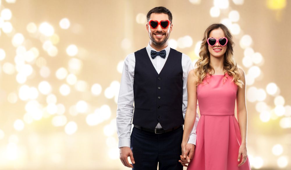 valentines day, love and people concept - happy couple in heart-shaped sunglasses over festive lights background. happy couple in heart-shaped sunglasses