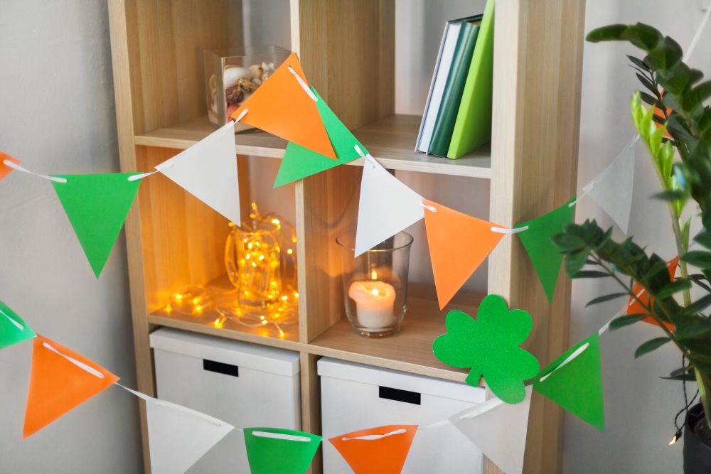 st patricks day, holidays and interior concept - close up of bookcase decorated by festive garland and shamrock for home party. home interior decorated for st patricks day party