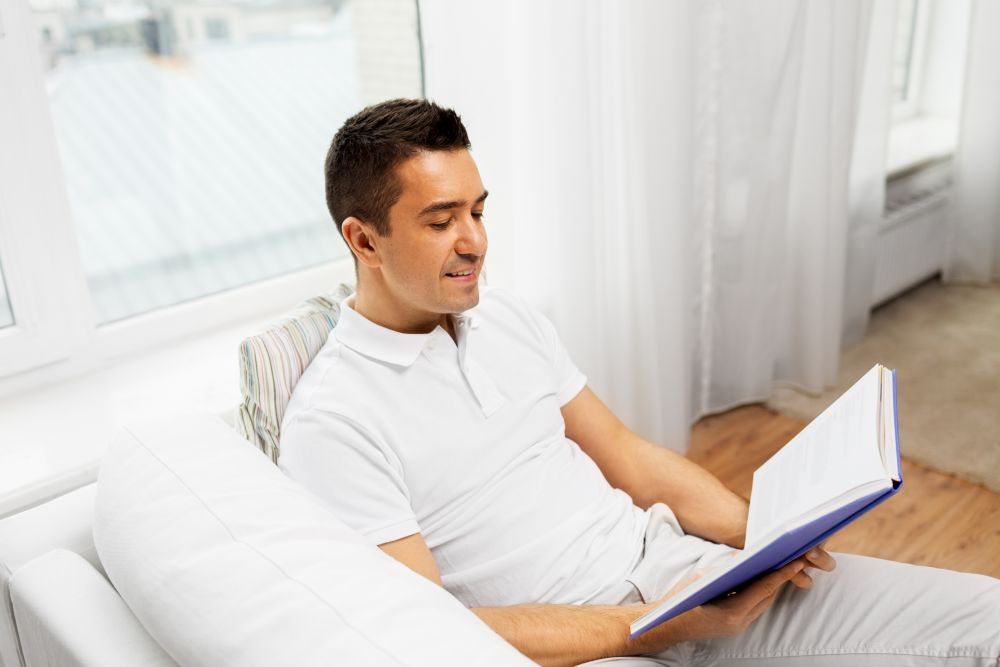leisure and people concept - happy man reading book at home. happy man reading book at home