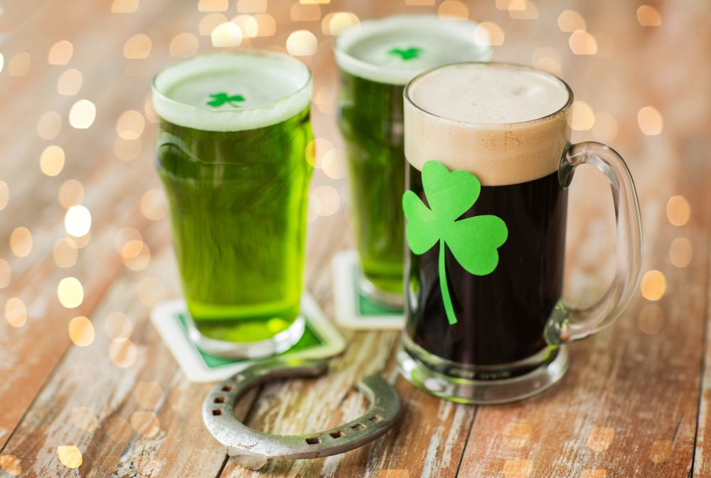 st patricks day, holidays and celebration concept - shamrock on glasses of beer and horseshoe on wooden table. shamrock on glass of beer and horseshoe on table