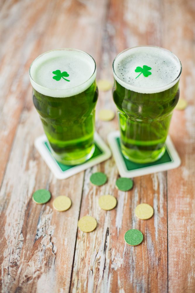 st patricks day, holidays and celebration concept - glasses of green beer with shamrock and gold coins on wooden table. glasses of green beer with shamrock and gold coins