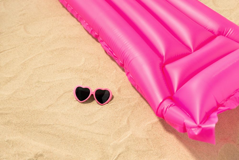 vacation and summer holidays concept - pink sunglasses and swimming mattress on beach sand. sunglasses and pink swimming mattress on beach