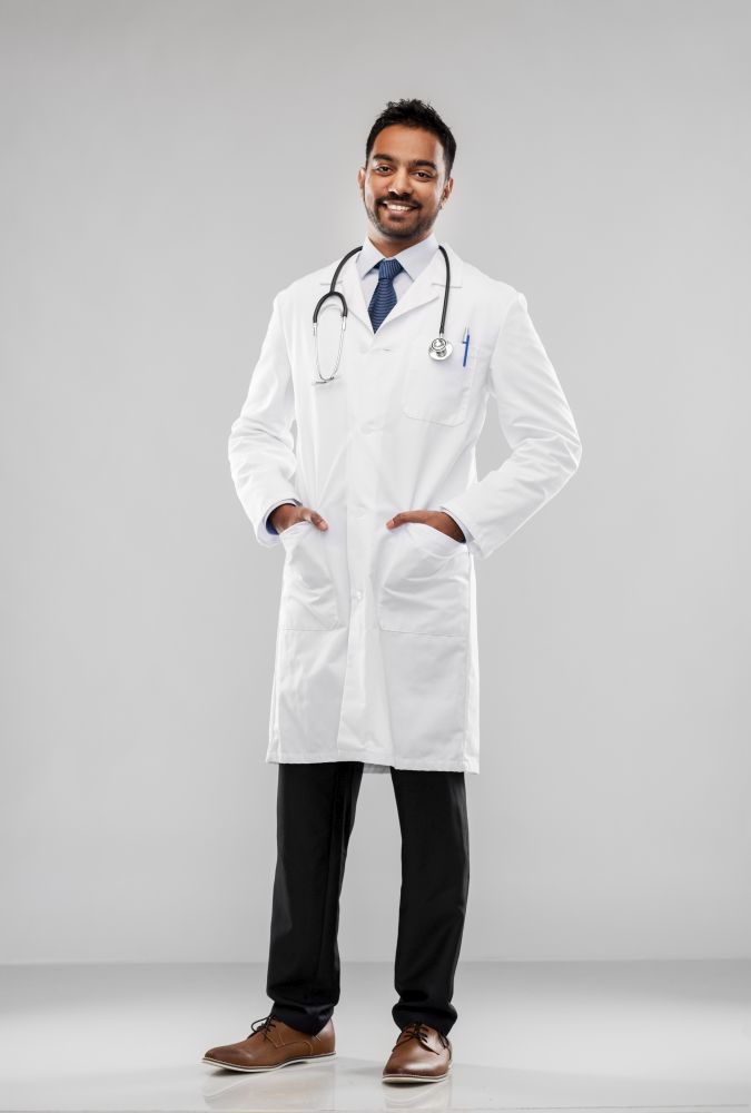medicine, profession and healthcare concept - smiling indian male doctor in white coat with stethoscope over grey background. smiling indian male doctor with stethoscope