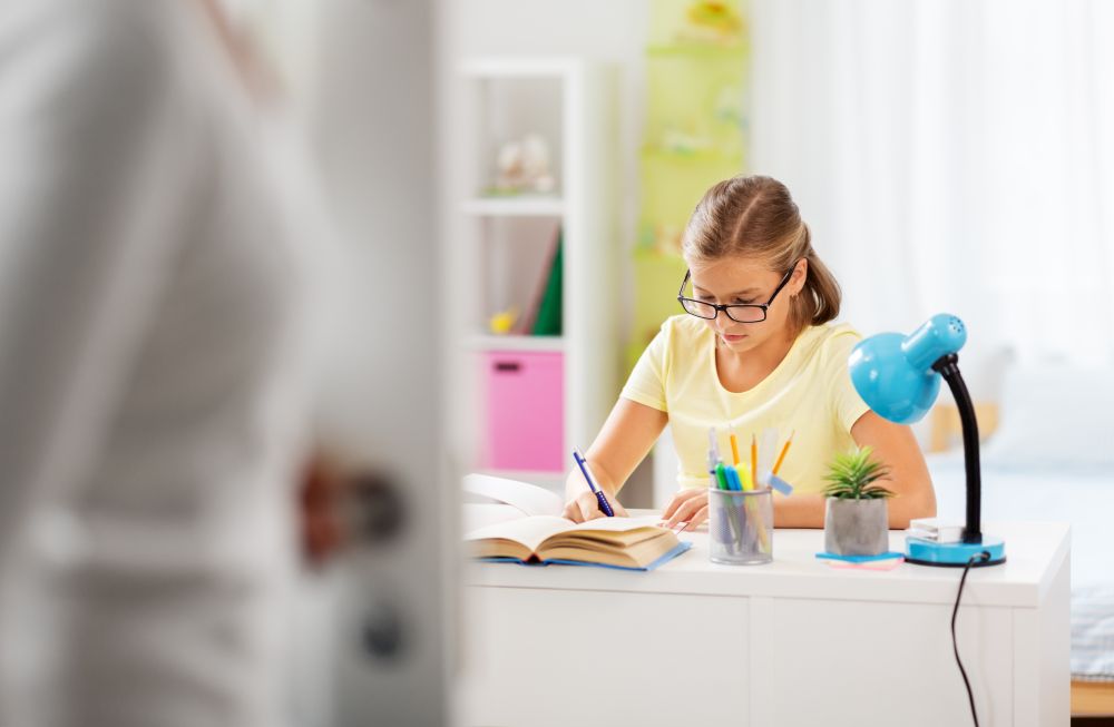 education, family and people concept - student girl doing homework and mother entering kids room. schoolgirl doing homework and mother entering room
