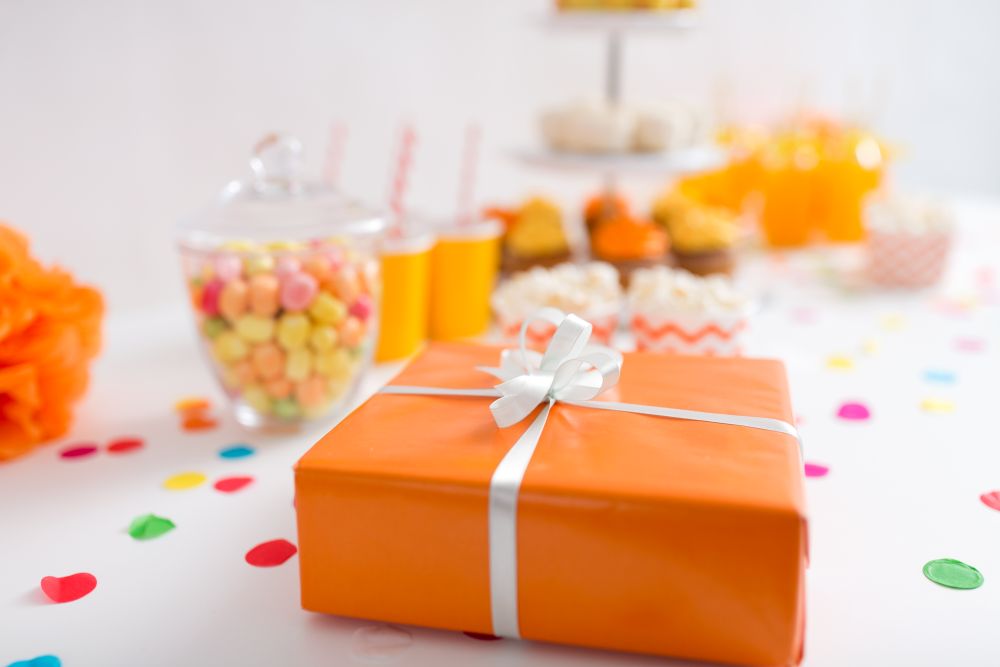 party and festive concept - close up of birthday present in orange wrap on table. birthday present in orange wrap on table at party