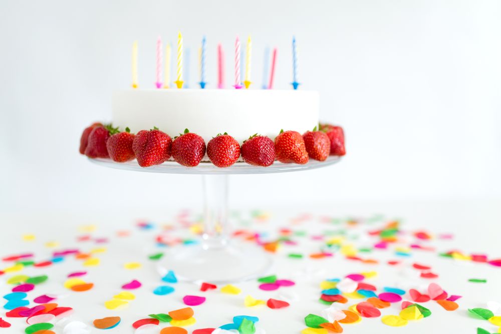 food, dessert and party concept - close up of birthday cake with candles and strawberries on stand. close up of birthday cake with candles on stand