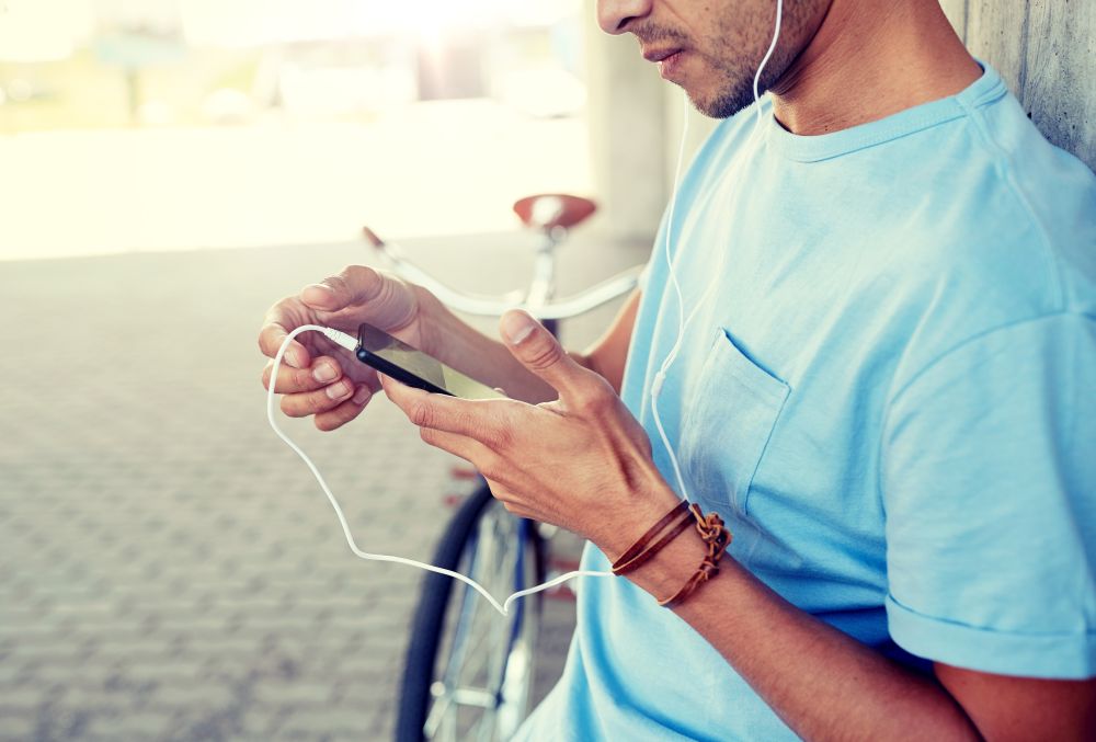 people, technology, leisure and lifestyle - close up of young hipster man with earphones, smartphone and bicycle listening to music. man with earphones and smartphone listening music