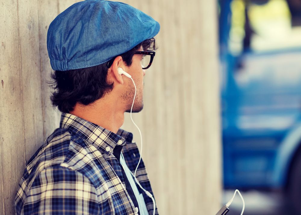 people, technology and lifestyle - happy young hipster man with earphones and smartphone listening to music. man with earphones and smartphone listening music